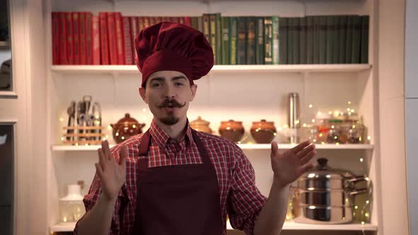 Cheerful Cook Stands in a Kitchen and Explains What He is Going to Do Gesticulating Actively