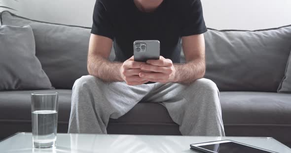 Anonymous Man Sitting on the Sofa in the Living Room and Uses a Modern Smartphone a Man Is Typing on