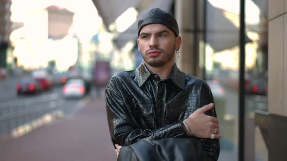 Front View Portrait of Chilling Young Gay Man Strolling on City Street Putting on Leather Jacket