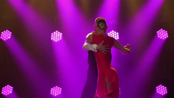 Passionate Young Couple Dancing Classic Argentine Tango in a Dark Studio with Bright Purple Lights