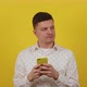 Cheerful Young Man in a White Shirt Uses a Phone on a Yellow Isolated Background - VideoHive Item for Sale