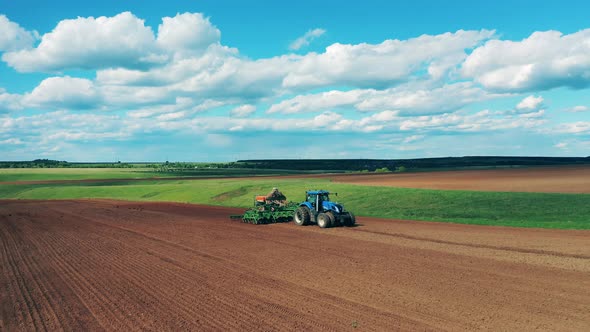 A Tractor Rides on Plowed Field, Sowing Seeds.