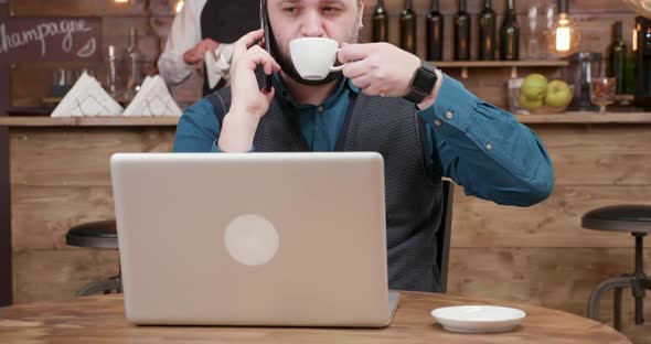 Handsome Young Freelancer Drinking Coffee in the Middle of a Phone Conversation