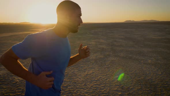 Athletic man working out with battle ropes on a dry lake at sunset