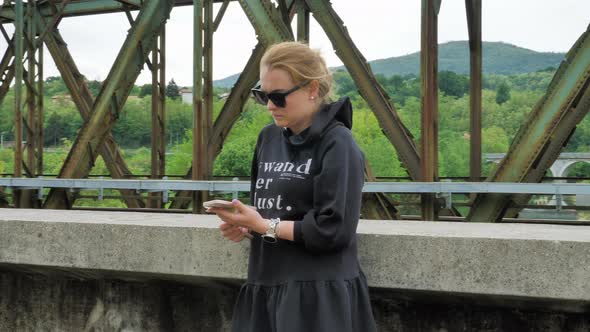 Slow motion shot of girl watching phone with the iron bridge in the background