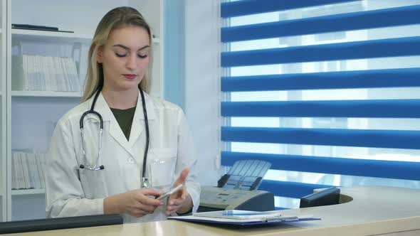 Pretty Nurse Using Tablet and Phone at Hospital Reception Desk