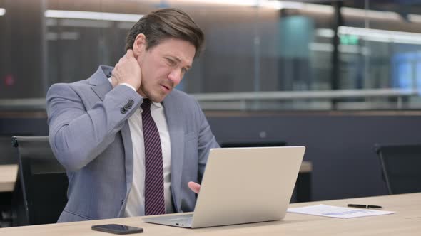 Middle Aged Businessman with Laptop having Neck Pain in Office 