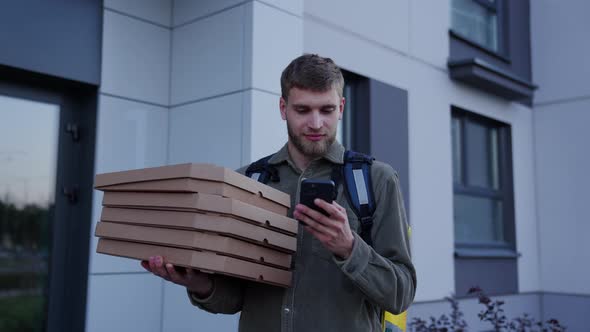 A Courier Man with a Yellow Backpack Holds Pizza Boxes in His Hands