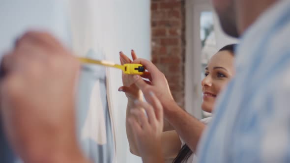 Young Happy Couple Measuring Wall in New Apartment