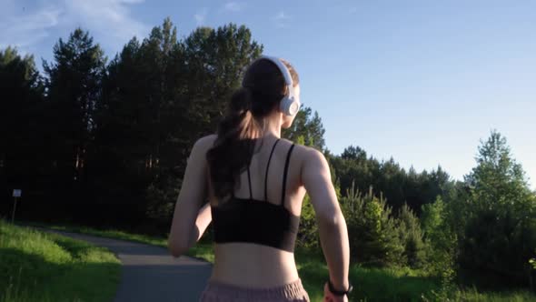 A Girl Jogs in the Park and Listens to Music on Headphones