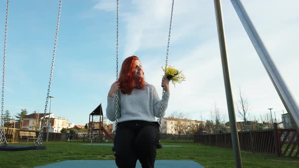 Young Beautiful Red Hair Girl Enjoys at the Park Playing with the Swing