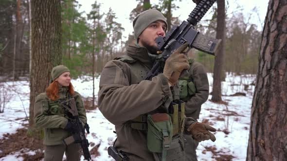 Confident Serious Man in Military Camouflage Raising Gun on Shoulder Looking at Camera with Blurred