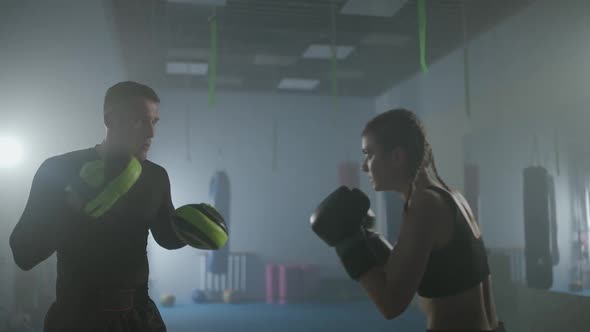 Young Woman Fighter Trains His Fast Punches Punching Focus Mitts Training Day with a Man Coach in