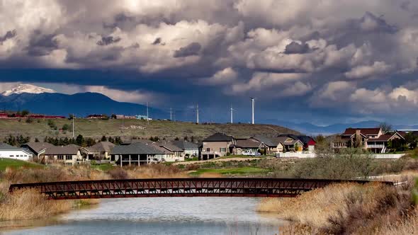 Static shot of wind turbines turning on a beautiful cloudy day in suburban setting with a river and