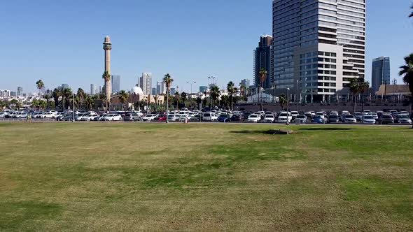 aerial rising forward drone shot of a parking lot full of cars at the edge of a park in Tel-Aviv. Ca