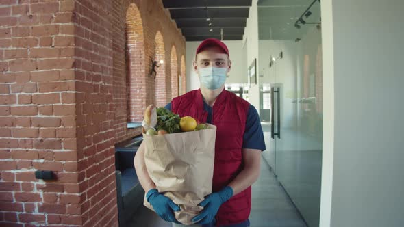 Postman or Delivery Man in Mask During Coronavirus Carry Small Box Food Deliver to Young Woman