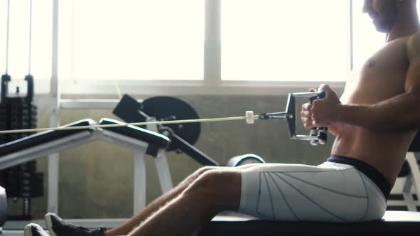 Shirtless Muscular Man Doing Seated Cable Row Exercise on Machine at the Gym