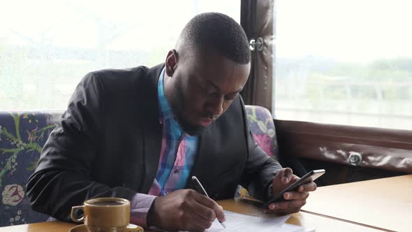 Afro American Businessman is Filling Documets in Summer Tent Cafe Looking in Smartphone