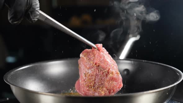 Cooking in Restaurant. Fine Cuisine. Chef Turning Meat with Cooking Tongs in Slow Motion. Juicy Meat