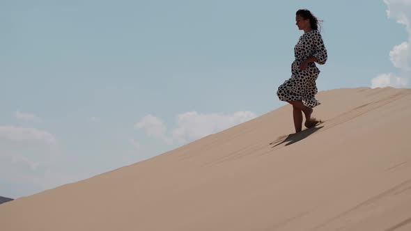 Girl in a Bright Dress Walking Barefoot Along the Dunes in the Desert