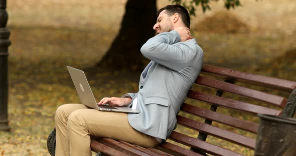 Pain in neck. Man in park, he experiences severe pain in neck. Work on laptop.