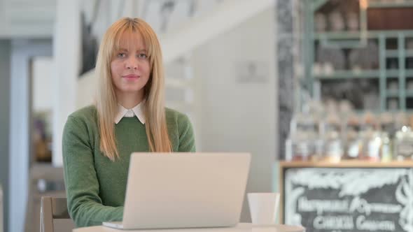 Young Woman Smiling at Camera While Working on Laptop in Cafe