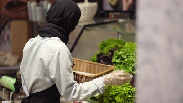 Woman in Scarf Refill the Fresh Greens on the Shelf at the Supermarket Side View