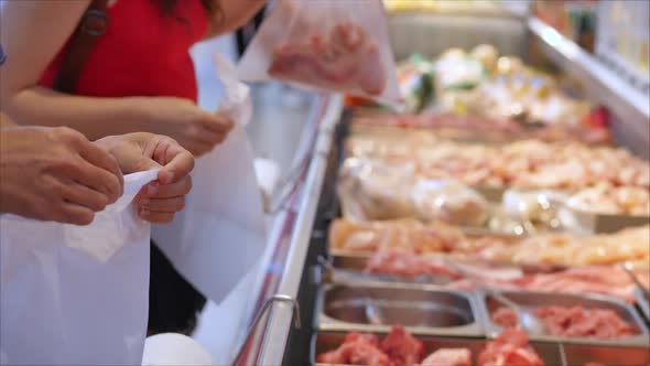 Buyers in the Supermarket in the Meat Department Are Picking Meat in Bags To Weigh and Make a