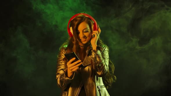 Portrait of Young Pretty Woman Is Dancing and Enjoying Music From Smartphone in Big Red Headphones