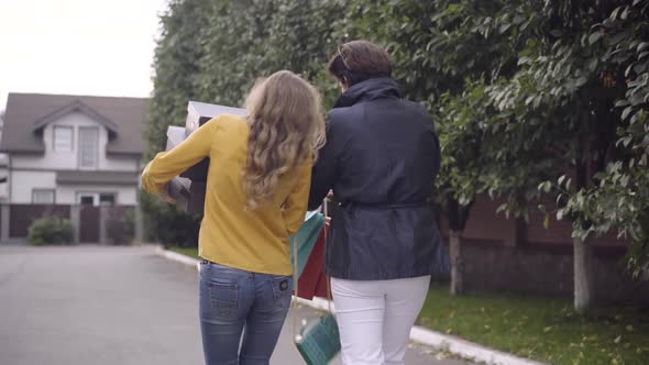 Back View of Stylish Young and Middleaged Women Walking Home on Black Friday