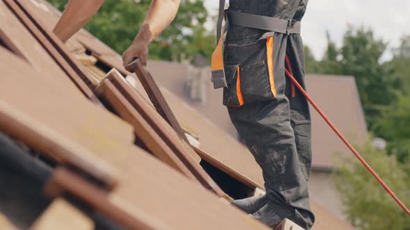 Roofing scene of worker on rooftop removing tiles. Working for solar installation company.