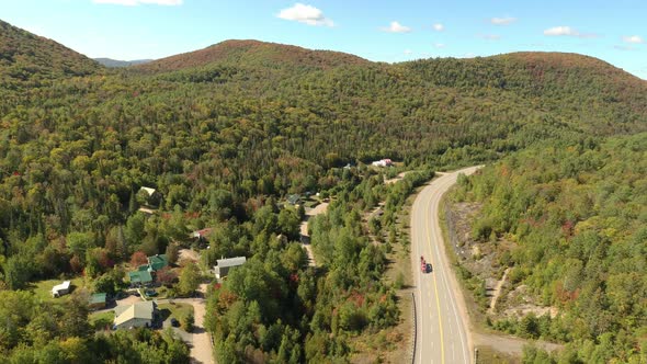 Countryside road with a few houses nearby seen by flying drone in a forest