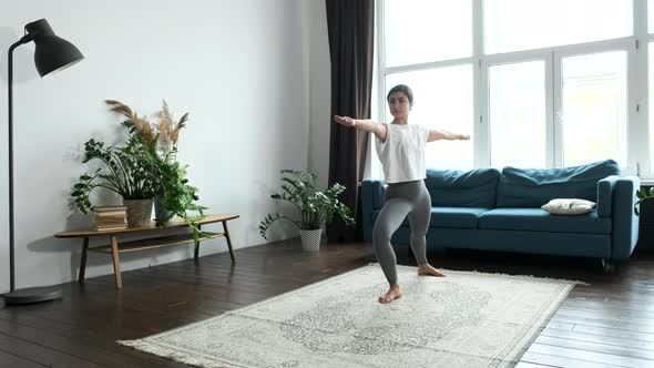 Young Indian Woman Doing Yoga Asanas While Standing On Floor Alone. Is At Home in A Bright Room