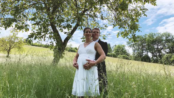 Happy groom and pregnant bride on a summer meadow