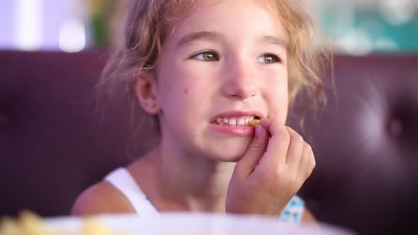 A 5-year-old girl is funny eating French fries in a cafe with her hands