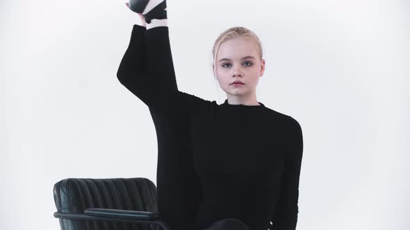 Young Blonde Woman Ballerina Sitting on the Chair and Raising Up Her Leg Up