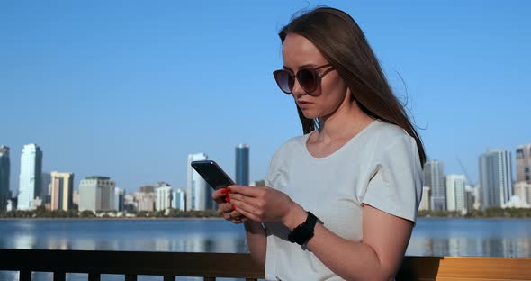 A Girl with Long Hair Dials a Message on the Smartphone at the Quay of Dubai