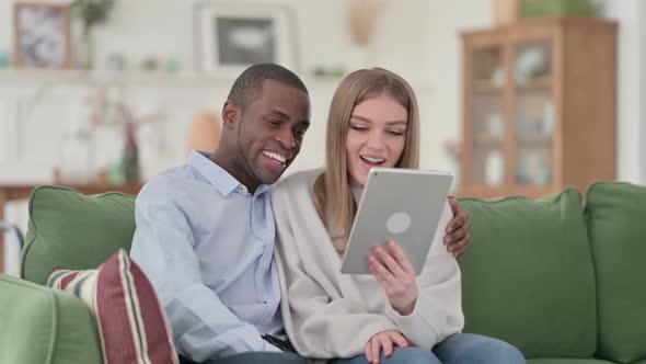 Mixed Race Couple Celebrating Success on Tablet at Home