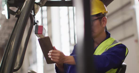 Asian male worker wearing safety suit with helmet using tablet in warehouse