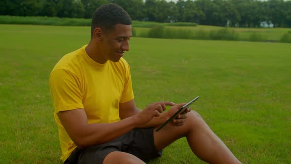 Cheerful Handsome Black Man Networking Online on Digital Tablet in Nature