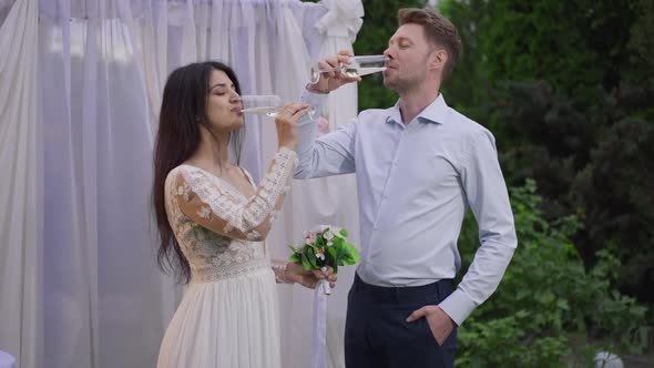 Happy Interracial Couple Drinking Champagne at Wedding Altar Outdoors Smiling