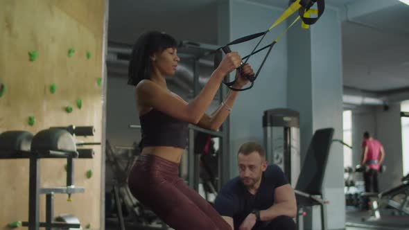 Woman Training Squats and Pull Up on TRX Trainer