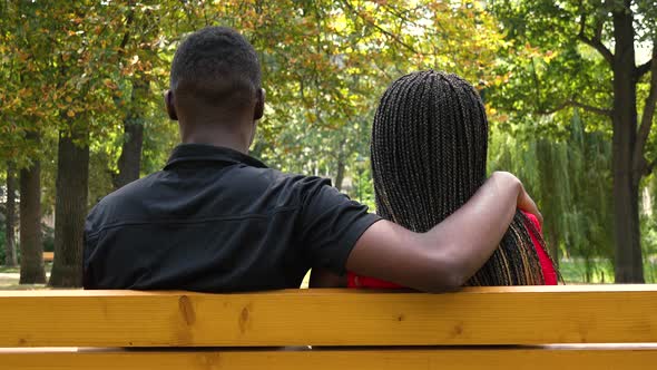 A Black Couple Sits on a Bench in a Park and Talks - View From Behind