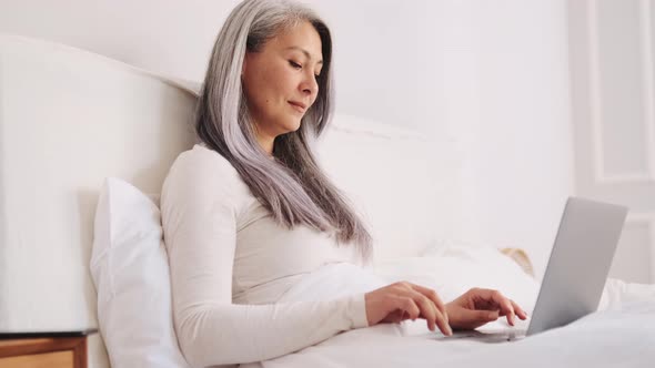 Happy Asian woman texting by laptop