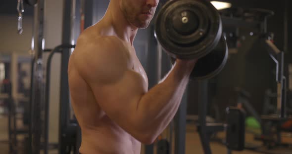 Athletic Shirtless Young Sports Man Doing Exercises with Dumbbell in Gym