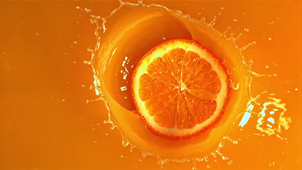 A Round Piece of Orange Falls Into the Orange Juice with Splashes