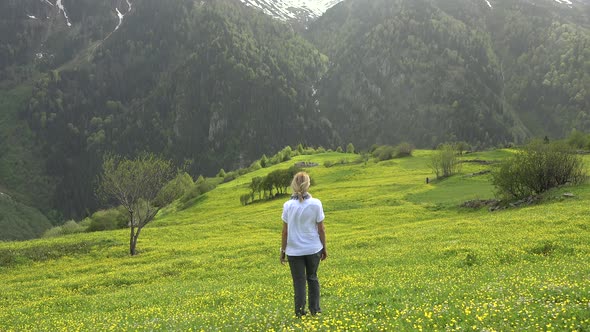 Blond Haired Alone Woman is Watching View in Yellow Flowery Meadow to Forest