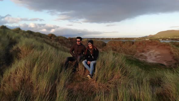 Flight Around a Young Couple Sitting in the Grass at Sunset