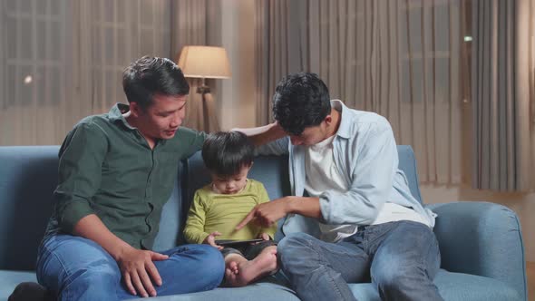 Asian Gay Fathers And Their Cute Son Relaxing On Couch And Using Mobile Phone