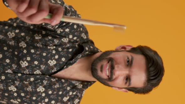 Attractive Young Latin Man in a Shirt Holding a Bamboo Toothbrush Showing It to the Camera